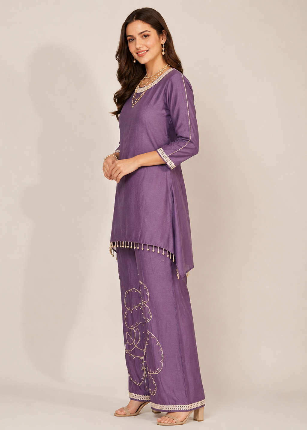 A woman modeling a purple traditional Indian outfit consisting of a kurta with three-quarter sleeves and matching wide-leg pants, featuring silver embroidery and bead trim, set against a plain beige studio background.