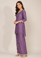 A woman modeling a purple traditional Indian outfit consisting of a kurta with three-quarter sleeves and matching wide-leg pants, featuring silver embroidery and bead trim, set against a plain beige studio background.