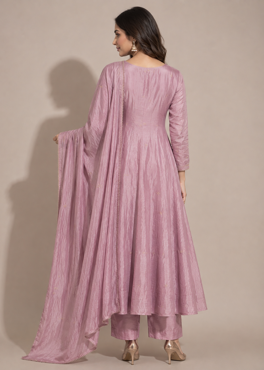 A woman modeling a dusty pink traditional Indian outfit with a long kurta, matching pants, and a draped dupatta, shown from the back against a solid beige studio background.