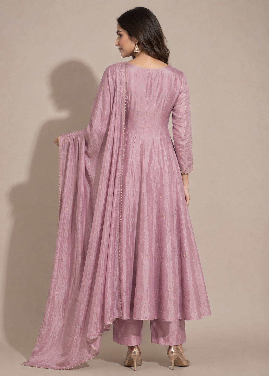 A woman modeling a dusty pink traditional Indian outfit with a long kurta, matching pants, and a draped dupatta, shown from the back against a solid beige studio background.