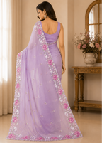 A woman wearing a lavender purple saree with pink floral embroidery and a matching embroidered border, shown from the back in an elegant indoor setting.