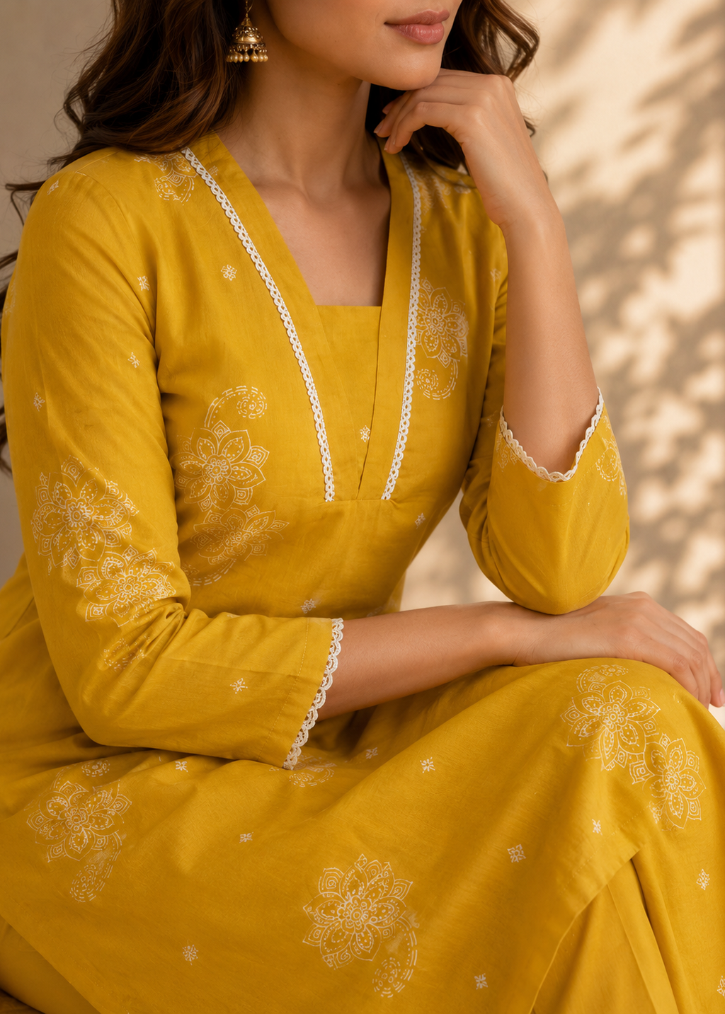 Woman wearing a mustard yellow traditional outfit with white embroidery sitting against a neutral background.