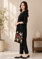Woman wearing a black outfit with floral embroidery in a bright room.