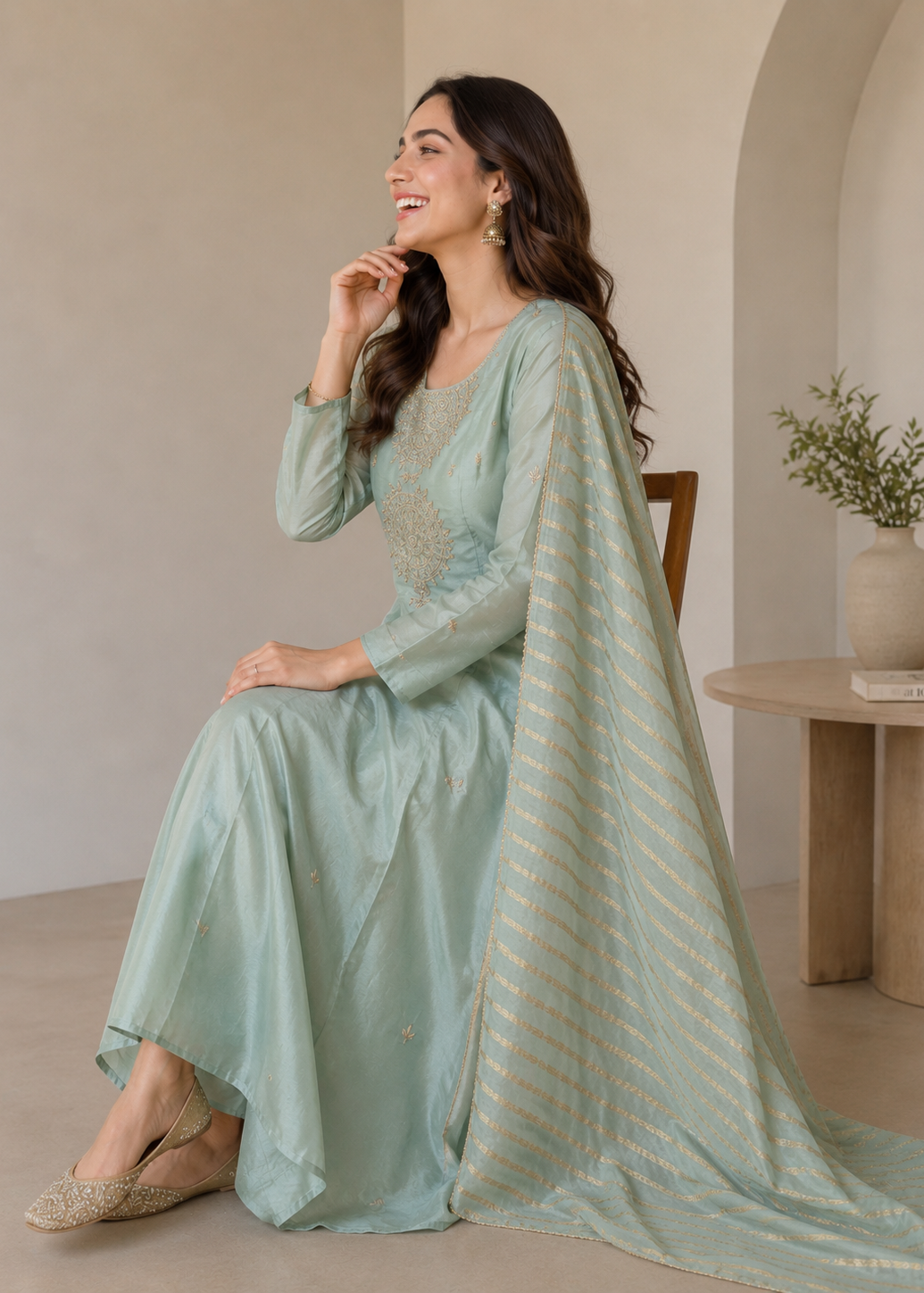 Woman in a light green traditional outfit with a matching dupatta, sitting indoors.
