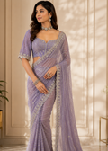 Woman wearing a lavender saree with intricate designs in an elegant indoor setting.