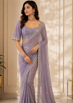 Woman wearing a lavender saree with intricate designs in an elegant indoor setting.