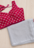 Red blouse with silver patterns and a gray saree with red tassels on a light wooden surface