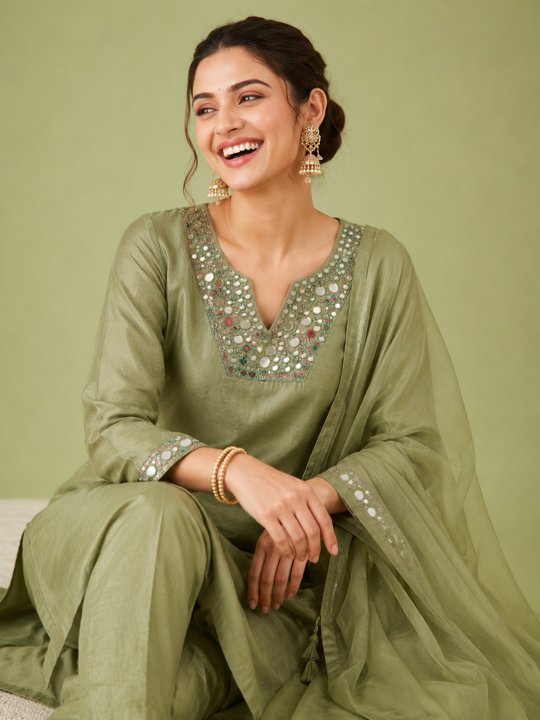 Woman wearing a green traditional outfit with sequin details against a light green background