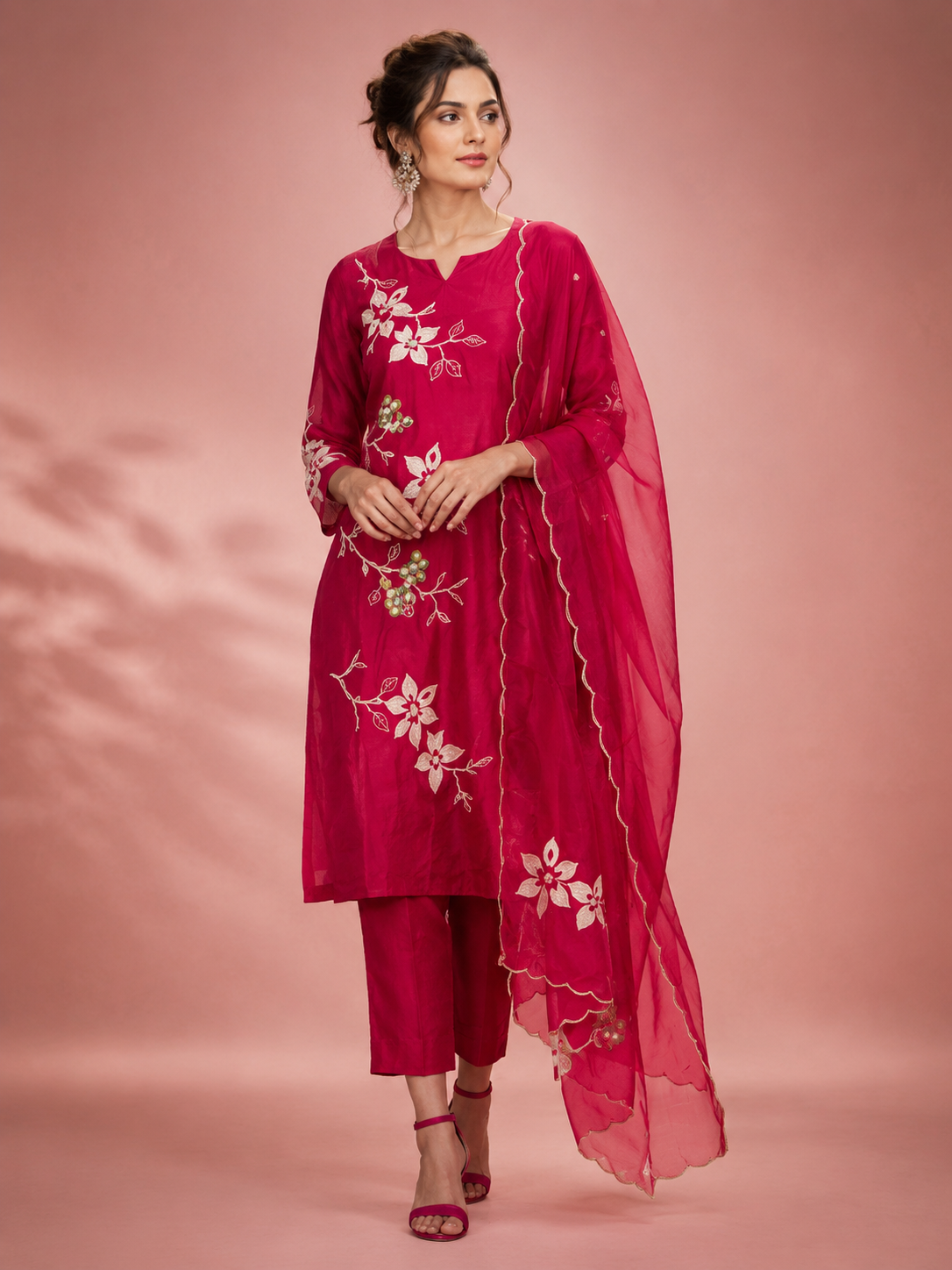 Woman wearing a pink embroidered outfit with a dupatta on a pink background