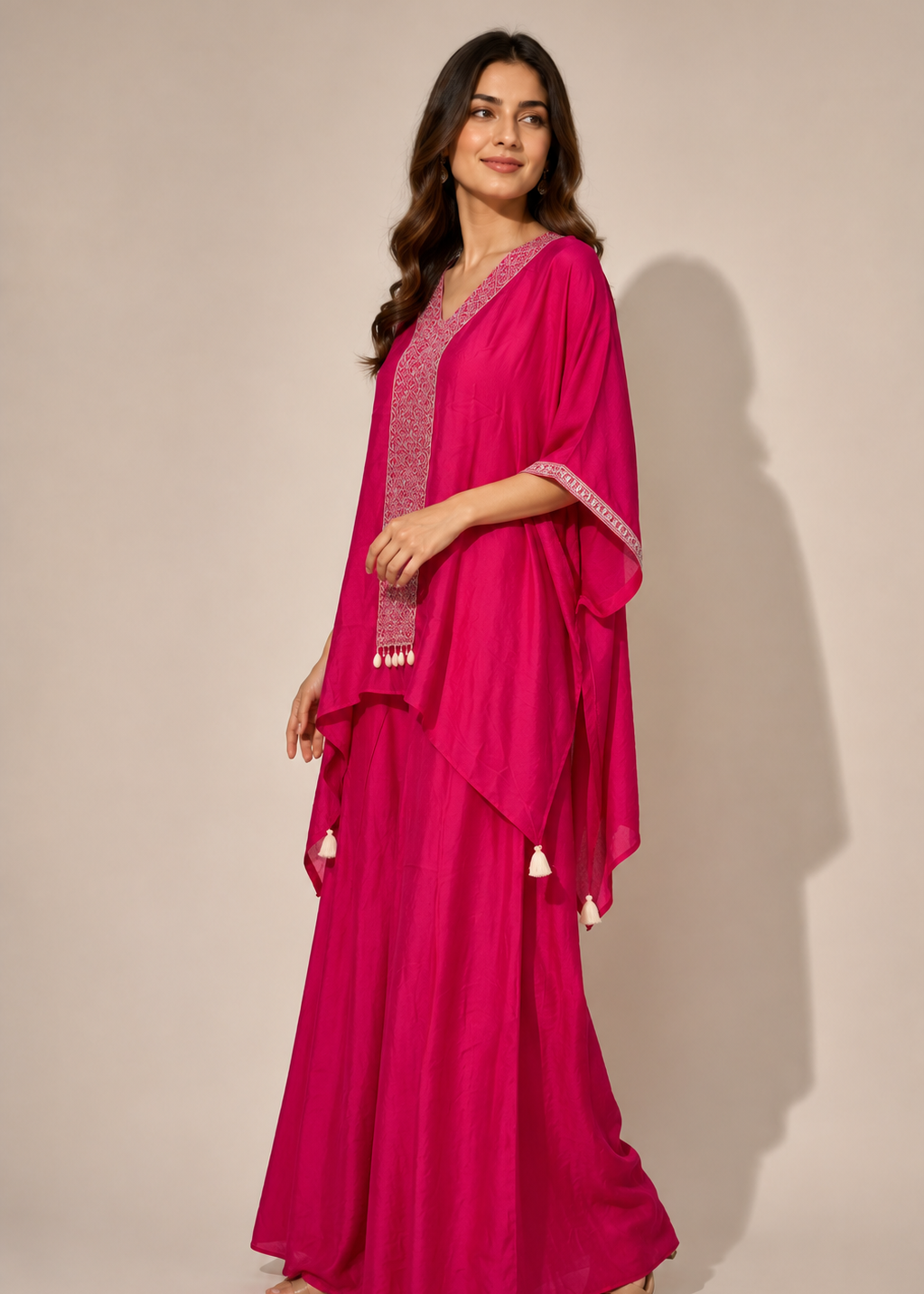 A woman modeling a bright magenta pink traditional outfit consisting of a long kurta with silver embroidery and a matching draped shawl with tassel details, set against a plain beige studio background.