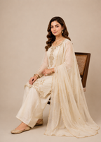 Woman in a cream traditional outfit sitting on a chair against a beige background