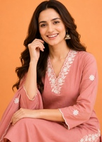 Woman wearing a pink embroidered dress against an orange background