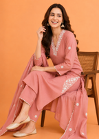 Woman in a pink traditional outfit with white embroidery sitting on an orange background