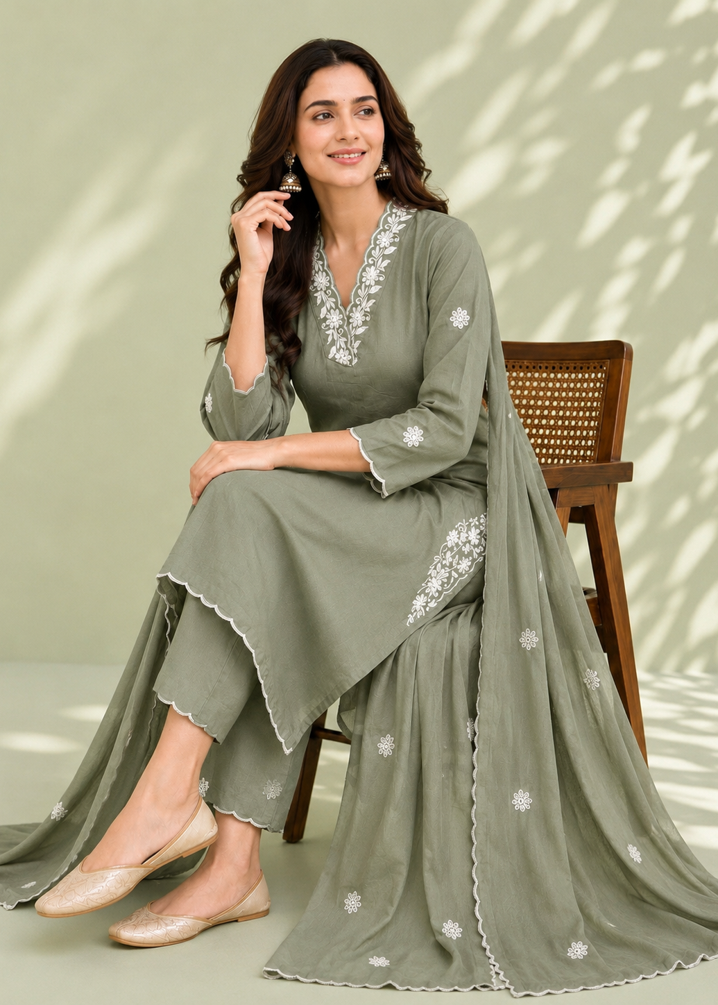 Woman in a green embroidered outfit sitting on a chair with a light background