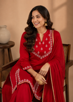 Woman in a red traditional outfit with white embroidery sitting on a wooden chair.