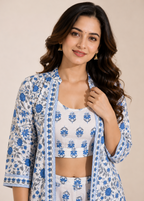 A woman modeling a white three-piece ethnic set featuring blue floral block prints, including a cropped tank top, matching trousers, and an open-front jacket.