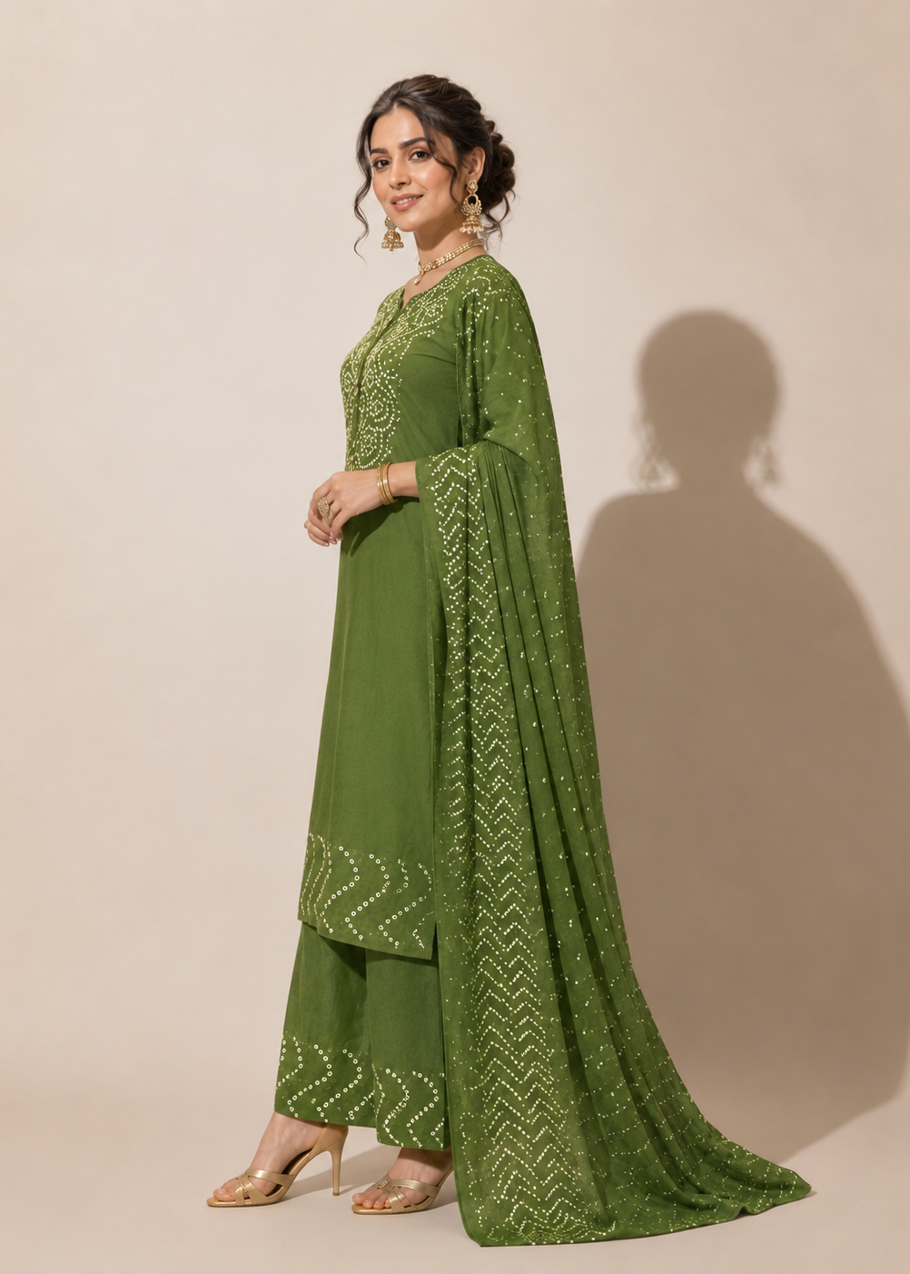A woman models a green traditional outfit with matching dupatta, featuring intricate white embroidery, set against a plain beige studio background with a soft shadow.