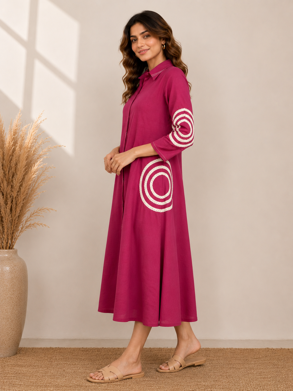 A woman modeling a magenta midi dress with white concentric circle patterns on the sleeves and skirt, standing in a neutral indoor setting.