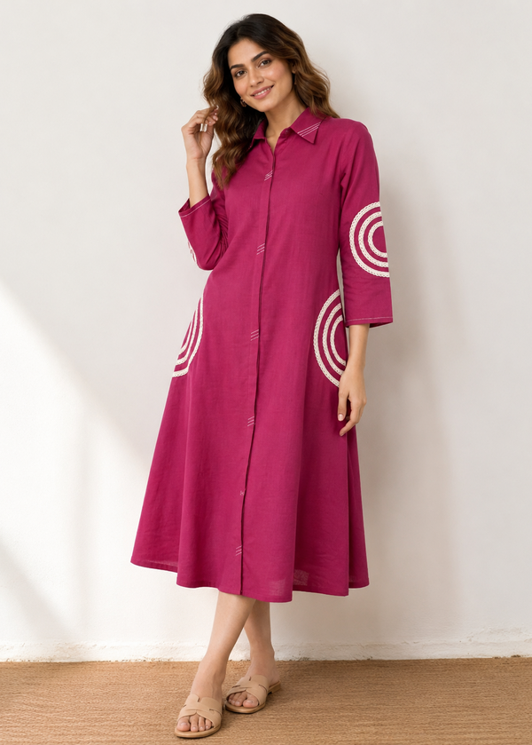 A woman modeling a magenta pink long-sleeve midi dress with white circular concentric pattern details on the sleeves and skirt, standing against a white wall.
