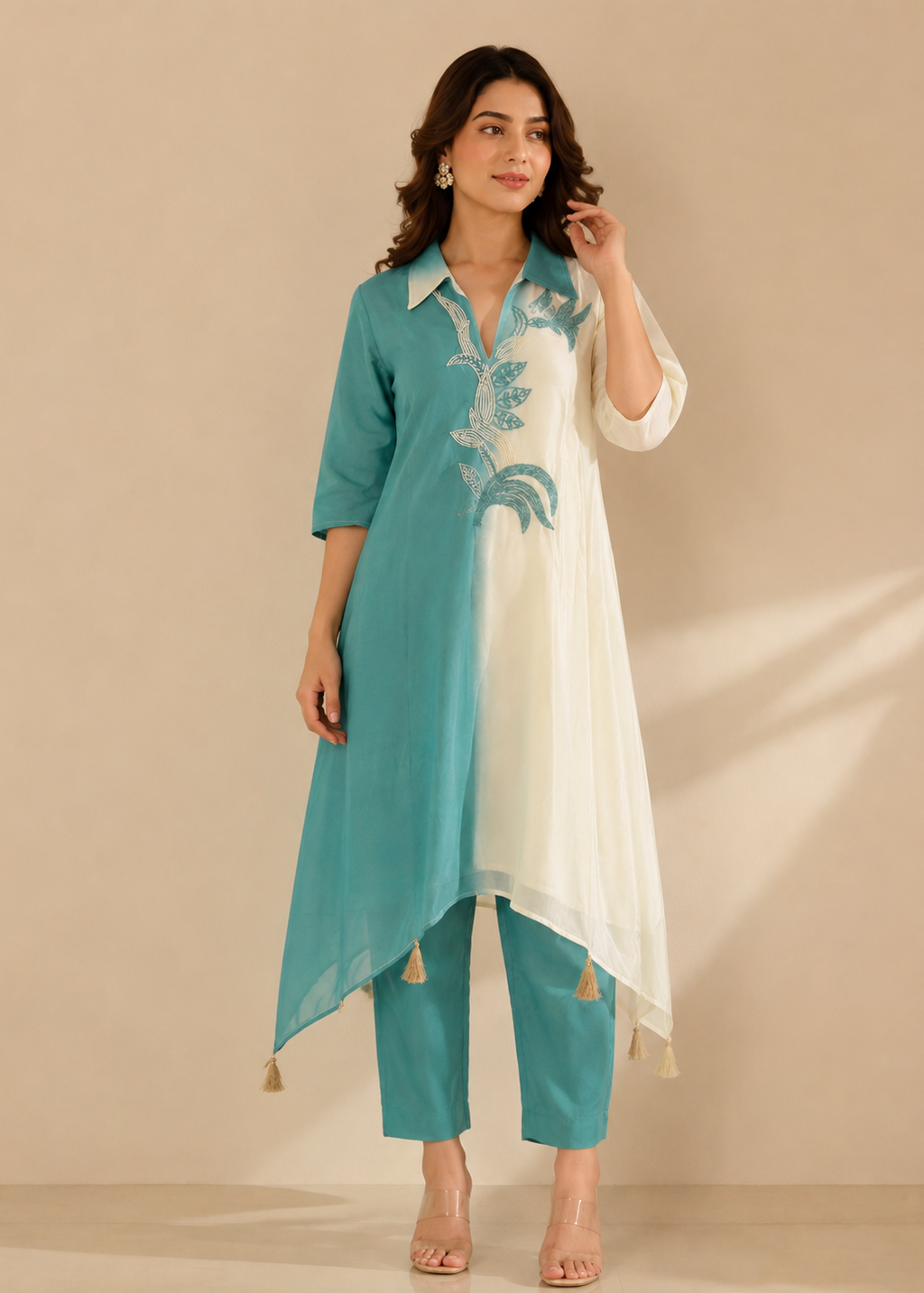 A woman models a teal and white embroidered kurta set with matching pants against a warm beige studio backdrop.