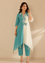 A woman models a teal and white embroidered kurta set with matching pants against a warm beige studio backdrop.
