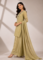 A woman modeling a traditional Indian salwar kameez suit in a light olive green color with a matching dupatta, standing against a neutral studio backdrop with soft shadows.
