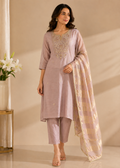 A woman models a light pink ethnic salwar kameez suit set with matching pants and a sheer patterned dupatta, set against a warm beige background with decorative white flowers on the left.