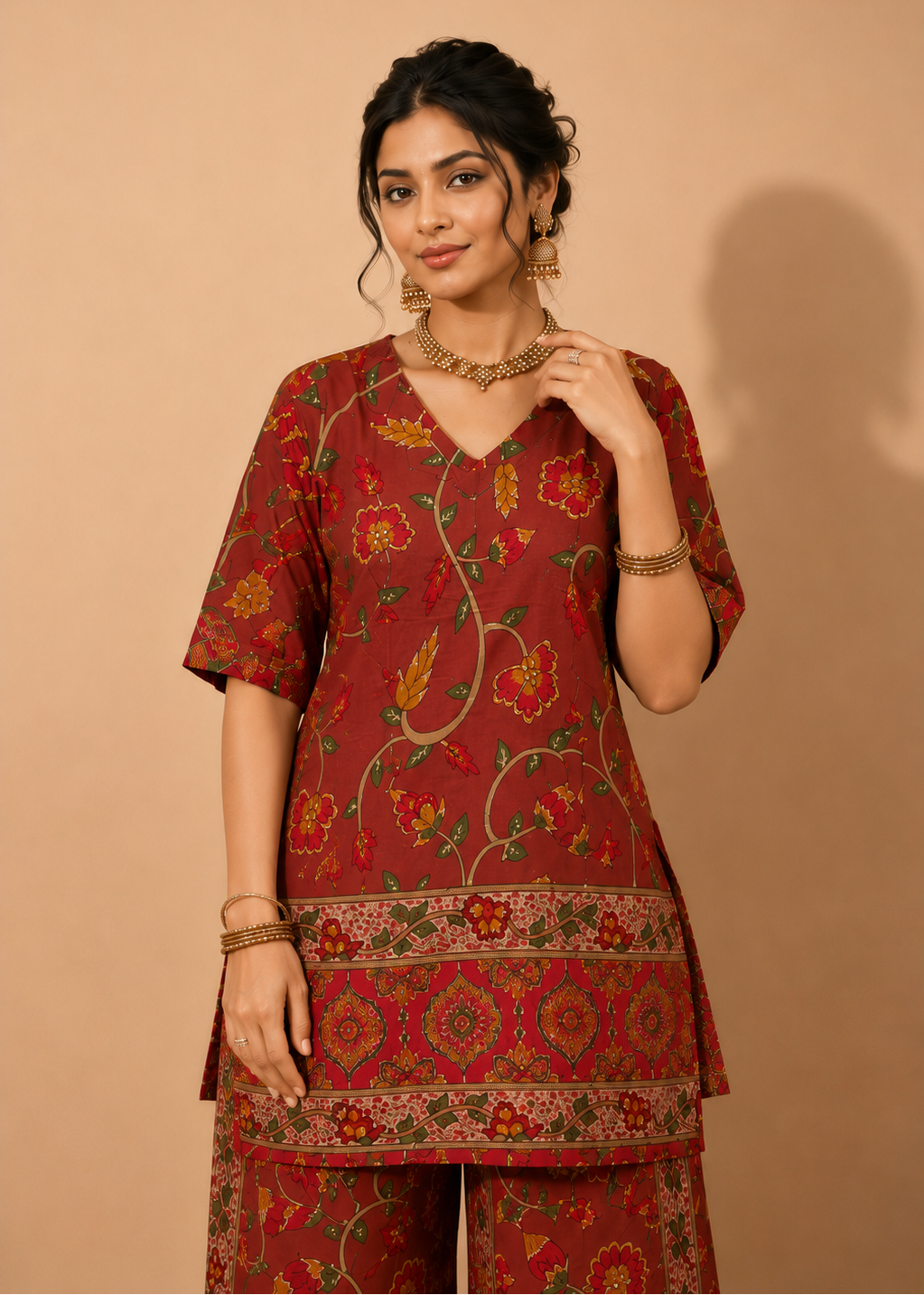 A woman models a rust-red three-piece kurta set with yellow, green, and orange floral block prints, set against a solid beige background.