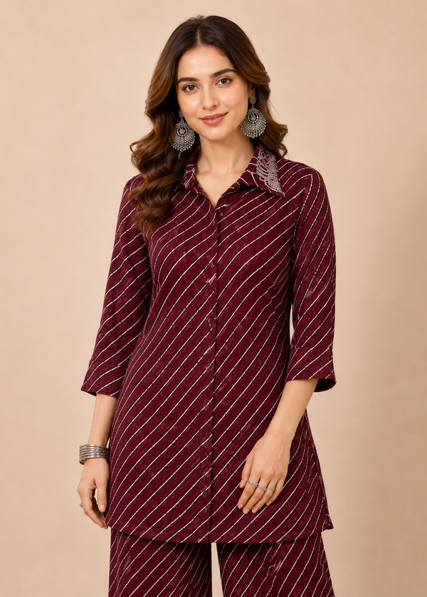 A woman modeling a matching deep maroon three-piece kurta set with thin white diagonal stripes, featuring a collared long-sleeve top, button-front styling, and coordinating trousers, set against a solid beige background.