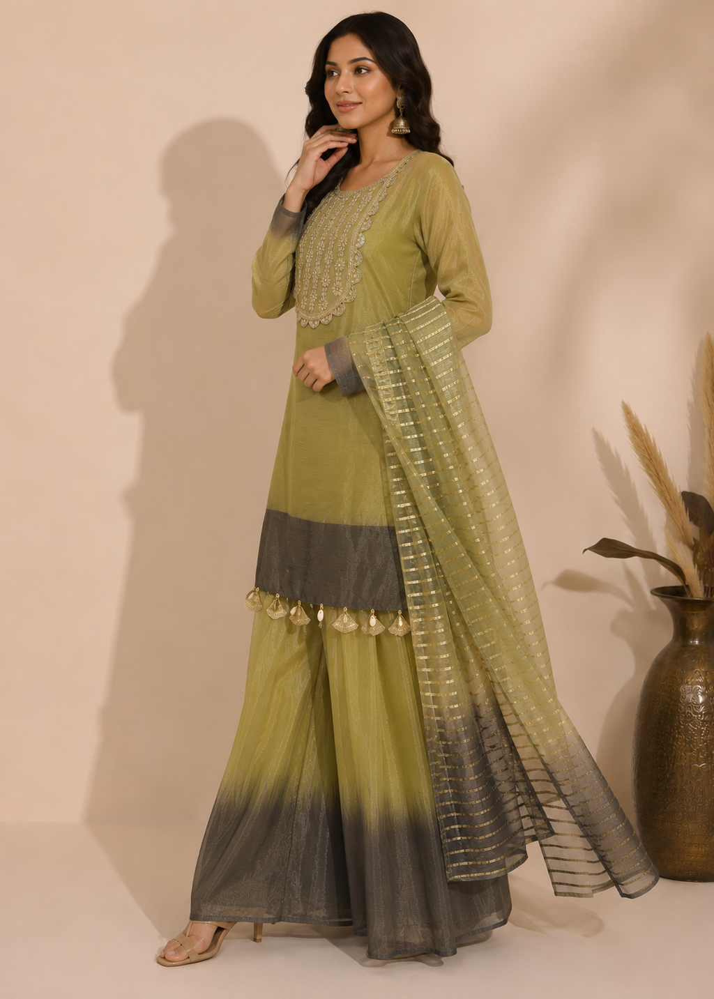 A woman models a traditional Indian outfit consisting of an olive green kurta with gold embroidery, wide-leg pleated pants with a dark-to-light gradient, and a matching sheer dupatta with gold patterns.