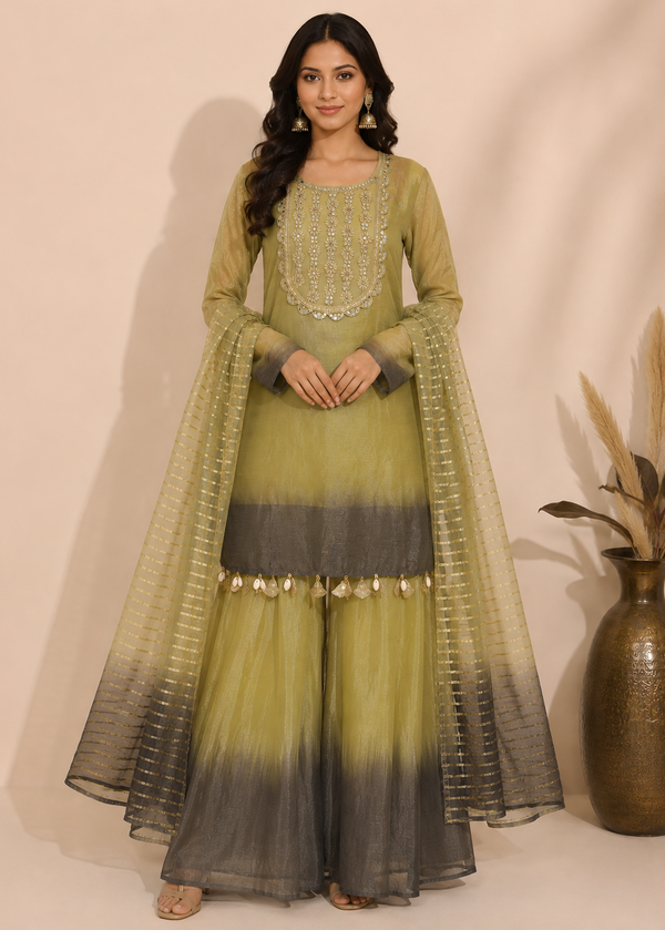 A woman models a traditional Indian outfit consisting of a sage green and dark gray ombre flared kurta with matching sheer dupatta, set against a plain beige background.