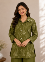 A woman modeling an olive green kurta with a beige abstract pattern, paired with matching olive green trousers, set against a warm beige background with soft window shadow patterns.