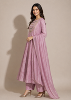 A woman modeling a dusty pink traditional Indian outfit consisting of a long kurta, matching trousers, and a draped dupatta, set against a solid beige studio background.