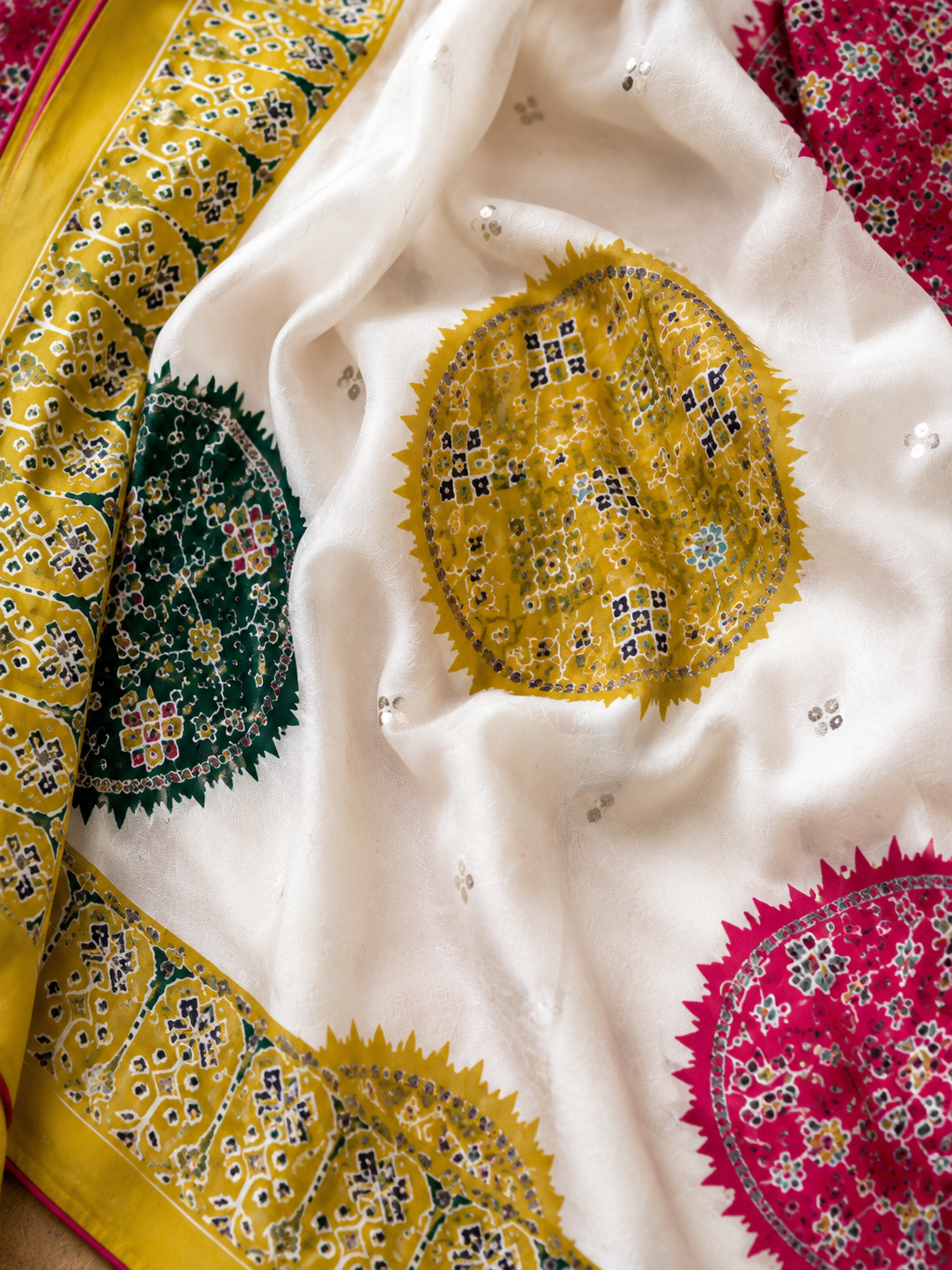 Close-up of a colorful fabric with circular patterns in yellow, green, and pink on a white background.