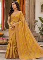 Woman in a yellow saree with a pattern, standing in an outdoor setting with decorative elements.