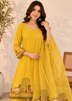 A woman models a bright yellow traditional Indian outfit with matching pants and a sheer dupatta featuring colorful animal and floral border prints, set against a softly lit indoor background.