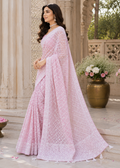 Woman in a pink saree standing outdoors with decorative elements.