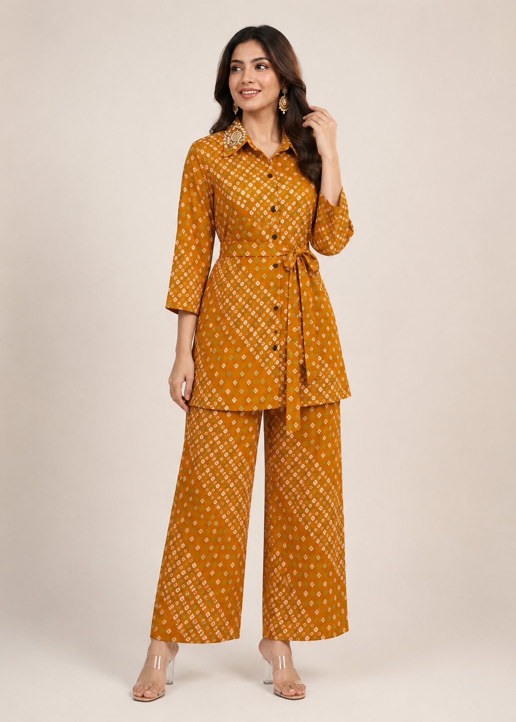 A woman modeling a mustard yellow two-piece kurta set with a white geometric pattern, featuring a long-sleeve button-up shirt and matching wide-leg pants, against a solid beige studio background.
