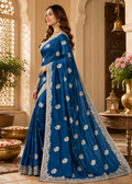 Woman wearing a blue saree with white patterns in an ornate indoor setting.