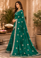 Woman wearing a teal saree with silver patterns in an ornate indoor setting.