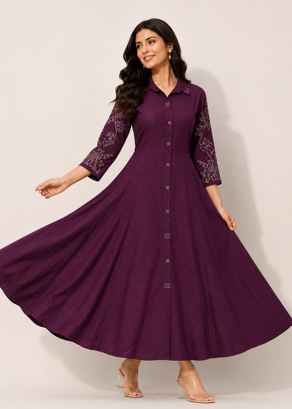 A woman modeling a long, flowing purple maxi dress with lace sleeves and a button-front bodice, photographed against a plain light beige studio background.