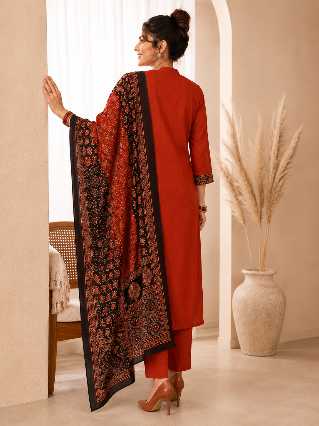 Woman in a red outfit with a patterned scarf in a room with a vase and chair.