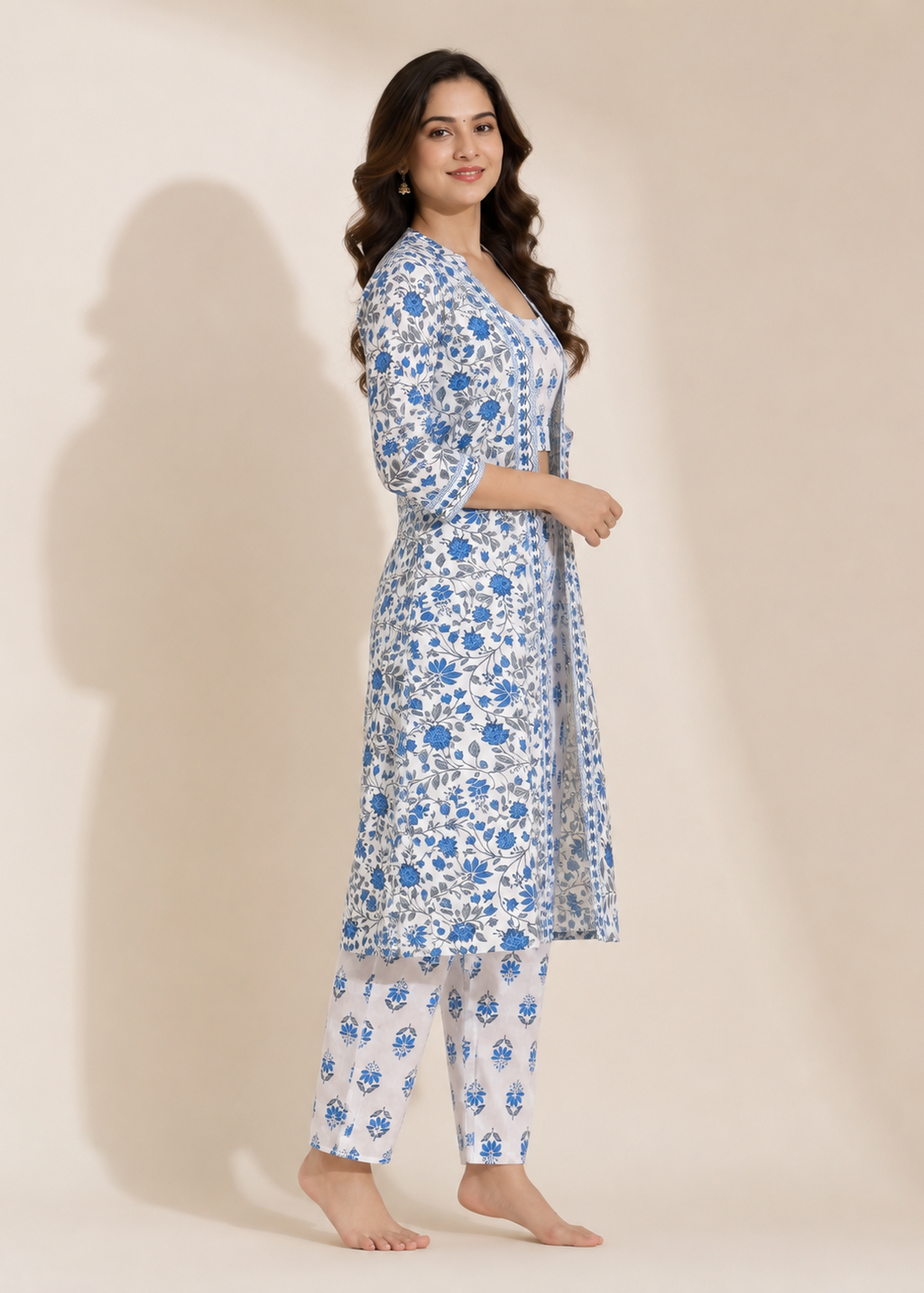 A woman modeling a blue and white floral print kurta set with matching pants against a warm beige studio background.