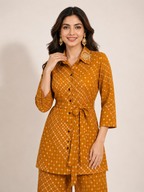 A woman modeling a mustard yellow printed kurta set with matching pants against a plain beige studio background.