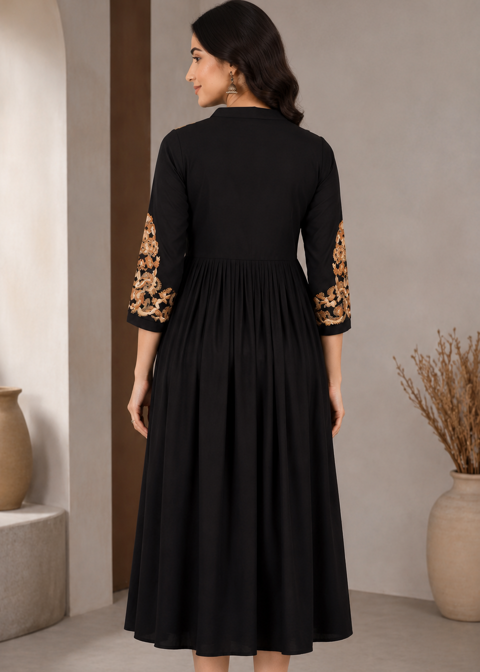 A woman wearing a black midi dress with 3/4 sleeves featuring gold and brown floral lace embroidery, shown from the back in a neutral indoor setting.