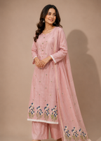 A woman modeling a light pink traditional Indian outfit consisting of a long kurta, matching pants, and a dupatta, decorated with floral embroidery near the hem and border.