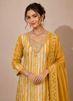 A woman models a traditional Indian outfit consisting of a mustard yellow and white striped kurta with silver embroidery, paired with a matching dupatta, against a solid beige background.