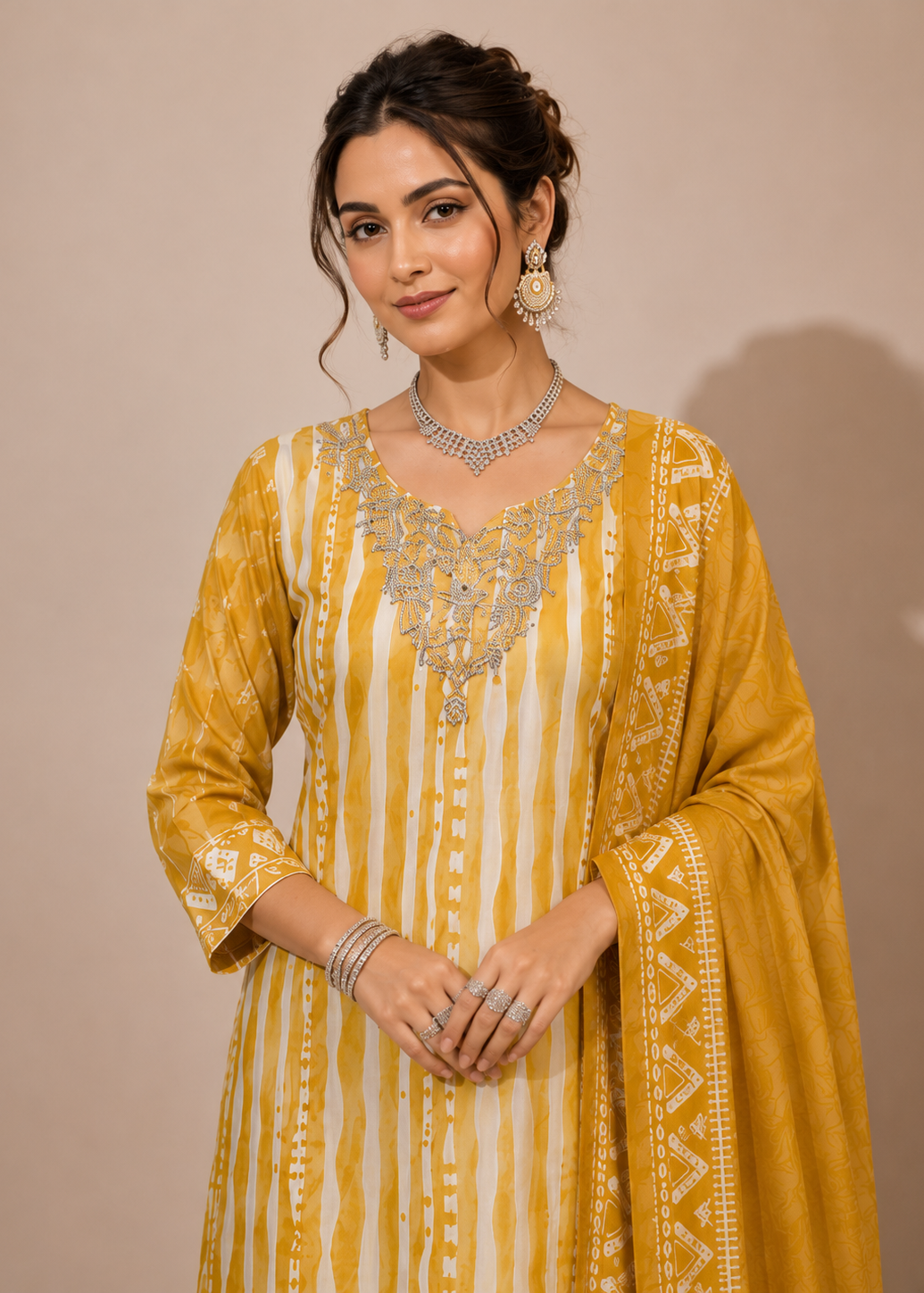 A woman models a traditional Indian outfit consisting of a mustard yellow and white striped kurta with silver embroidery, paired with a matching dupatta, against a solid beige background.