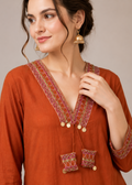 Woman wearing an orange embroidered top with a plain background
