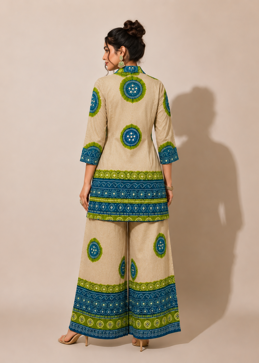 A woman stands with her back to the camera wearing a beige two-piece kurta set with blue and green printed patterns, photographed against a solid beige studio background.